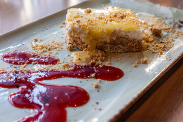 A dessert with a sauce and crumbs on served on a long plate with a raspberry sauce.