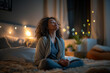 © SnapVault - A woman in cozy sleepwear sits cross-legged on her bed, meditating amidst a softly lit bedroom. String lights and indoor plants create a peaceful, serene atmosphere,relaxation and mindfulness.