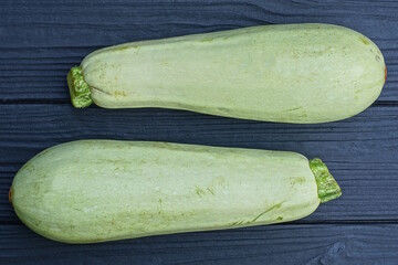 two big green fresh zucchini lie on a black wooden table