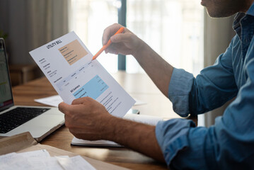 Man reviewing utility bill with a pen at home office desk. Concept of household expenses, family budget, and financial management 