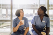 © Maskot - Smiling senior female doctor holding glass while talking with colleague during coffee break at hospital