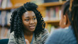 © Wanida - A young woman with curly hair is talking to another woman in a library