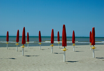 Empty beach with fine sand and folded red sun umbrellas by the Adriatic Sea in Italy in summer.