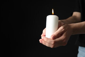 Wall Mural - Woman holding burning candle on black background, closeup. Space for text