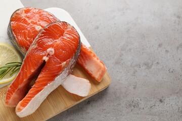 Wall Mural - Board with fresh salmon steaks, rosemary and lemon on grey textured table, closeup. Space for text