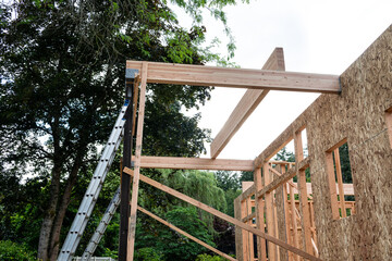 Wall Mural - New house construction in residential neighborhood, job site detail of back of home wood framing, vertical support beams with aluminum extension ladders and wood glue laminate beams
