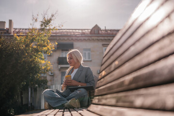 Wall Mural - A woman sitting on a bench with a cell phone in her hand. She is wearing a suit and she is working on her phone.