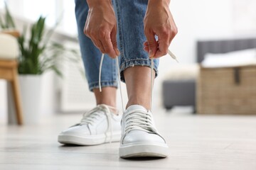 Wall Mural - Woman tying shoelace of white sneaker indoors, closeup