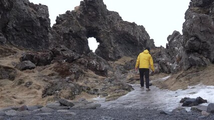 Wall Mural - A hiker with a backpack on Djupalonssandur beach on the Snaefellsnes peninsula in winter in Iceland. Wearing a yellow windbreaker