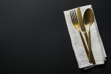 Wall Mural - Elegant golden cutlery and napkin on black background, top view. Space for text