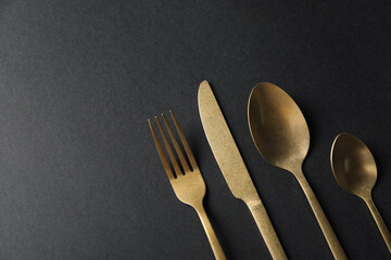 Poster - Elegant golden cutlery on black background, flat lay. Space for text