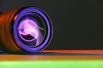 Wall Mural - Modern camera lens in neon lights on table, closeup. Space for text