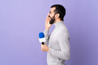 © luismolinero - Adult reporter man with beard holding a microphone over isolated purple background shouting with mouth wide open to the side