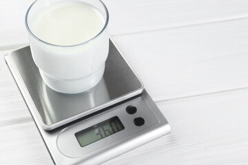 Poster - Kitchen scale with glass of milk on white wooden table, closeup. Space for text