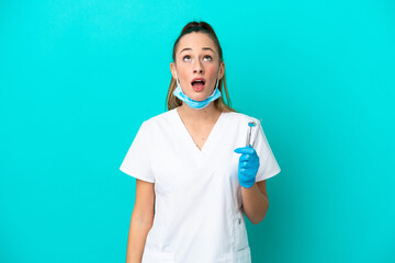 Wall Mural - Dentist caucasian woman holding tools isolated on blue background looking up and with surprised expression