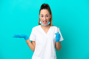 Wall Mural - Dentist caucasian woman holding tools isolated on blue background with shocked facial expression