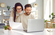 © Studio Romantic - Cheerful young couple using laptop and analyzing their finances with paper document. Smiling husband and wife using online banking service at home or receiving positive decision from bank by email
