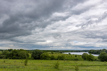 a cloudy sky with a field of grass and trees in the background