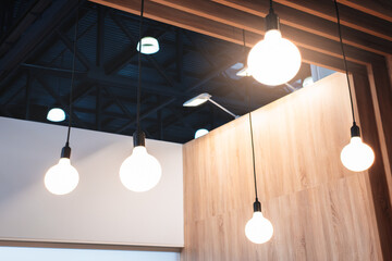Poster - A row of white light bulbs hanging from the ceiling. The bulbs are evenly spaced and are all lit up. The room has a modern and clean look