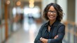 © Ananncee Media - A Black female teacher stands confidently, smiling in a vibrant school hallway
