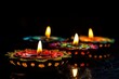 © Dzikrul Husnani - Group of decorated diyas on black background during Diwali, generative ai