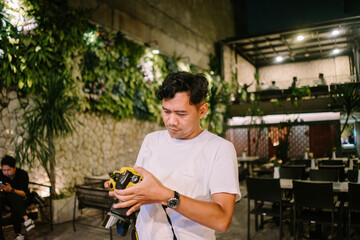 A tan-skinned Asian man is focused on photographing an object in front of him, capturing the moment