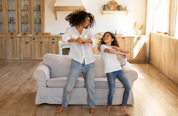 Overjoyed mom play dancing with funny preteen girl child, happy mother have fun entertain with daughter jump move to rhythm at home