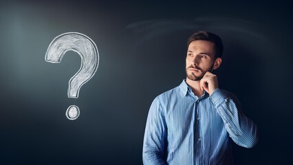 Concept: question, cognition, learning, intelligence. A man stands in front of a dark chalkboard, a question mark is drawn on the board with chalk.