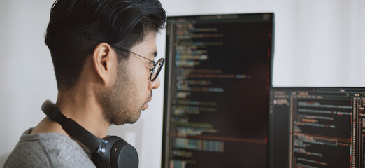 Young adult Asian male software developer coding program on desktop computer. Man work from home, remote working, freelance programmer job, smart digital nomad lifestyle concept