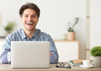 Poster - Man Sitting At Laptop And Laughing Looking At Camera Indoor. Empty Space For Text