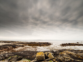 Wall Mural - A beach with a rocky shoreline and a calm ocean. The sky is cloudy and the water is a deep blue. Galway bay, Ireland. Burren mountains in the background. Travel and tourism. Irish landscape.