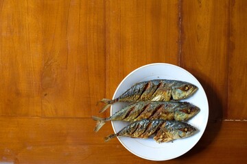 Fried mackerel in a white plate on a wooden table, healthy seafood concept, copy space.