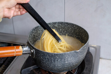 A woman cooks making Italian spaghetti pasta at gas stove in wok pan pot in boiling water, Culinary. Food background.