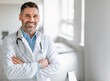 © Prostock-studio - Portrait of friendly middle aged european male doctor in workwear with stethoscope on neck posing with folded arms in clinic interior, looking and smiling at camera, free space