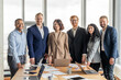 © Prostock-studio - A group of diverse business professionals stand in a modern office space, smiling for a photograph. The team consists of both men and women. They are dressed in business attire