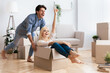 © Prostock-studio - A woman sits in a cardboard box while a man pushes her through a new house, both laughing.