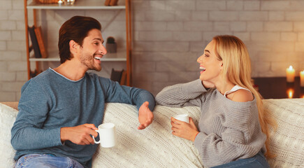 Wall Mural - Happy Couple Spending Time Together Drinking Tea And Talking Sitting On Sofa At Home. Selective Focus