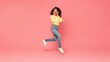 © Prostock-studio - African American young woman with dark curly hair jumps in the air with her hands on her cheeks. She is looking at the camera with a surprised expression. The background is a bright pink.