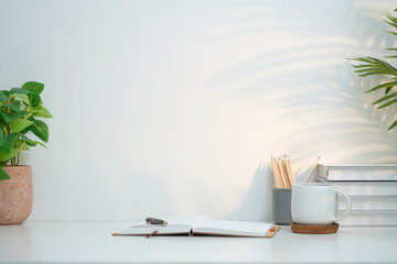Aufkleber - A clean and inviting minimalist workspace setup featuring a white desk against a pale wall. On the left side, a lush green potted plant adds a touch of nature and freshness to the space.