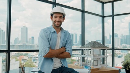 Wall Mural - Caucasian architect engineer with safety helmet placed project plan on table while sitting with arm folded. Smart interior designer crossing arm while sitting on table with house model. Tracery