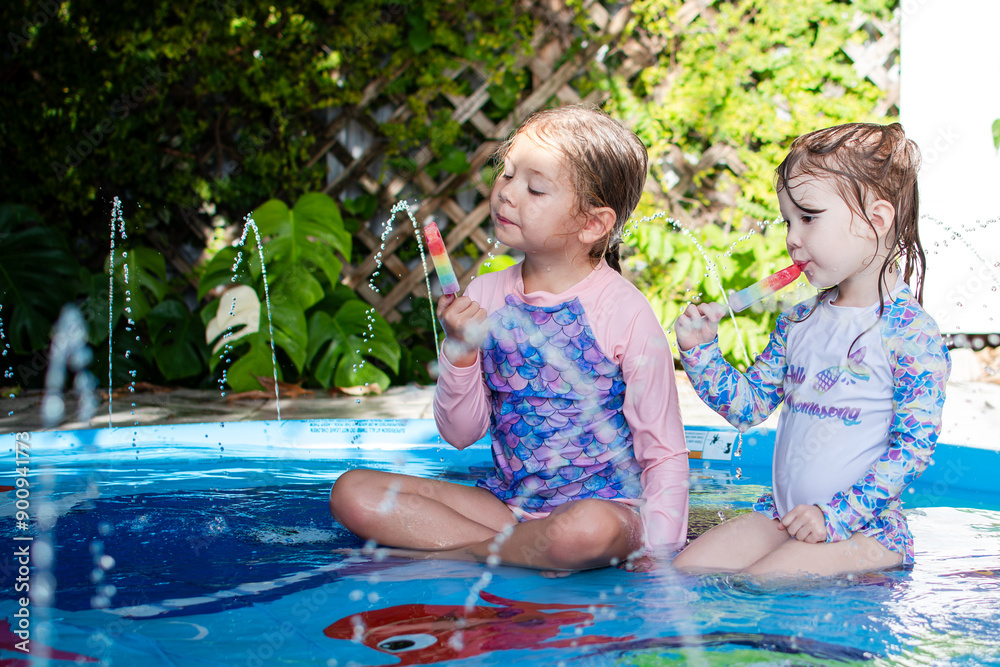 Two cute Caucasian children eating rainbow popsicle in a pool. Kids ...