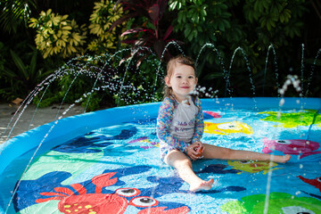 Cute Caucasian little girl playing in a kiddie pool. Summer fun concept. Enjoying summer at the pool. Smiling child at the splash pad