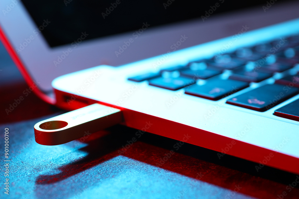 Modern laptop with metallic USB flash drive on black table, closeup