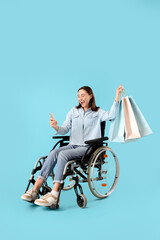 Sticker - Happy young woman in wheelchair with mobile phone and shopping bags on blue background