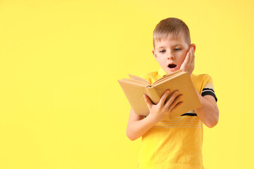 Wall Mural - Shocked little boy with book on yellow background