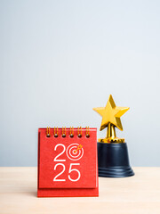 Wall Mural - Happy new year 2025 background. 2025 numbers with target icon on red small desk calendar standing near golden star prize trophy on white background, vertical style. Business goal and success concept.