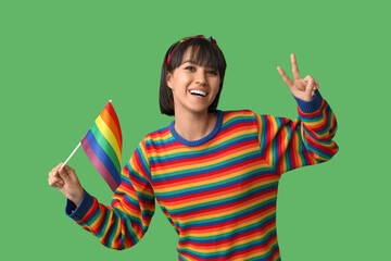 Wall Mural - Beautiful young woman with LGBT flag showing heart gesture on green background