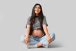 © Pixel-Shot - Beautiful young pregnant woman sitting on grey background