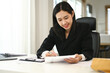 © Prathankarnpap - Smiling asian female employee examining documents at her workplace