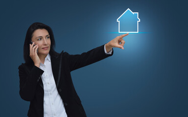 Poster - Businesswoman talking on her cell phone and pointing finger to house icon with copy space over light blue background, Business real estate concept